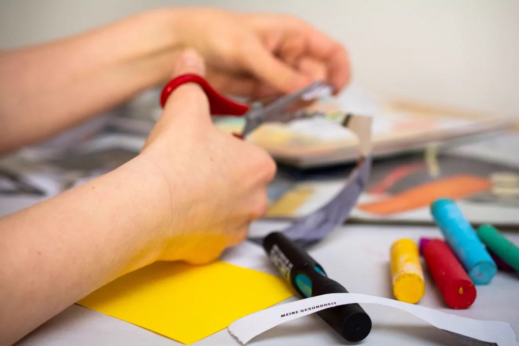 H&auml;nde schneiden Papier mit einer Schere, daneben bunte Marker beim Prototyping im Design Thinking