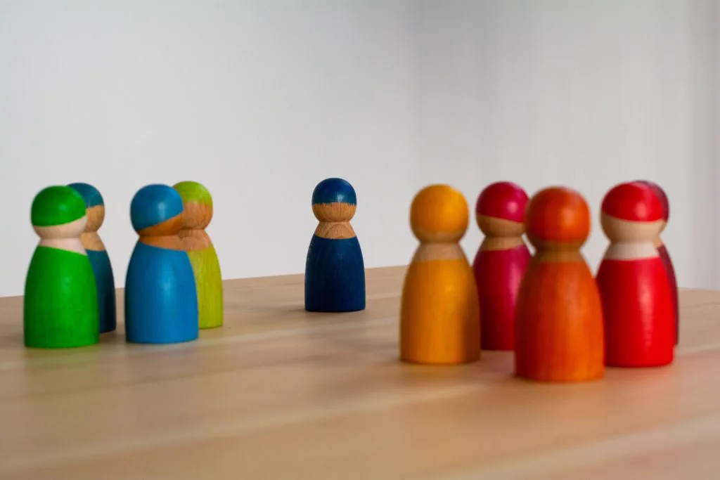 Bunte Holzfiguren in zwei Gruppen gegen&uuml;ber einer einzelnen Figur als Sinnbild f&uuml;r Konfliktmoderation