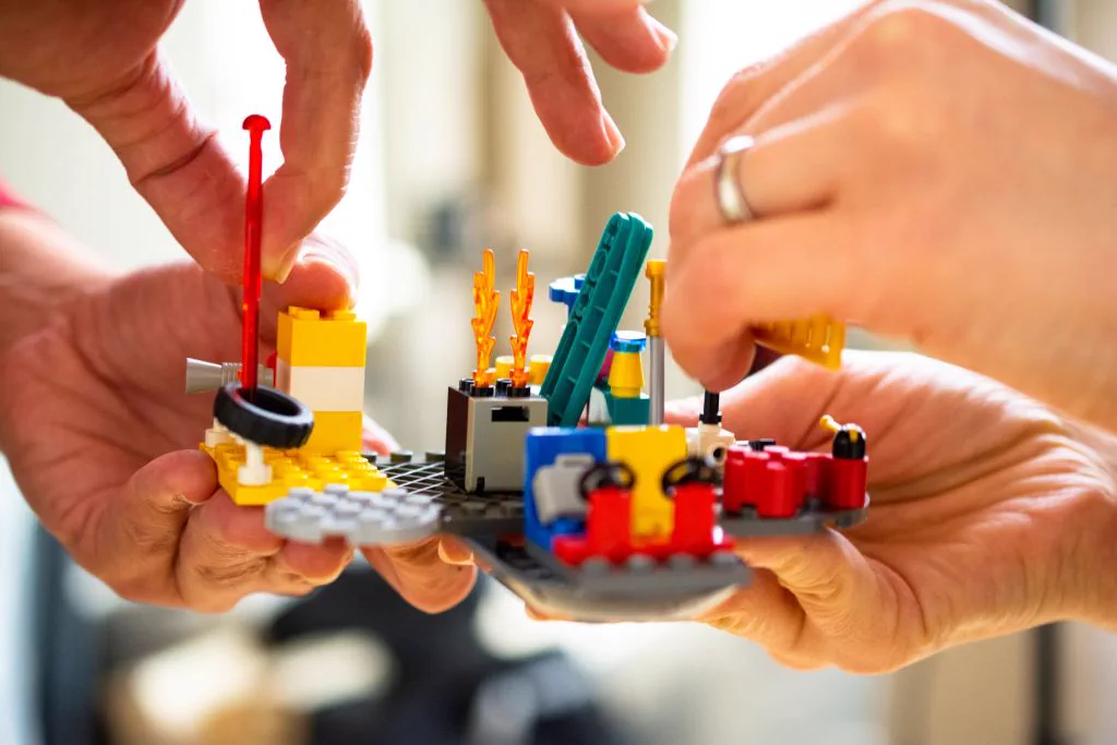 Zwei H&auml;nde bauen gemeinsam ein kleines LEGO-Modell in der Organisationsentwicklung